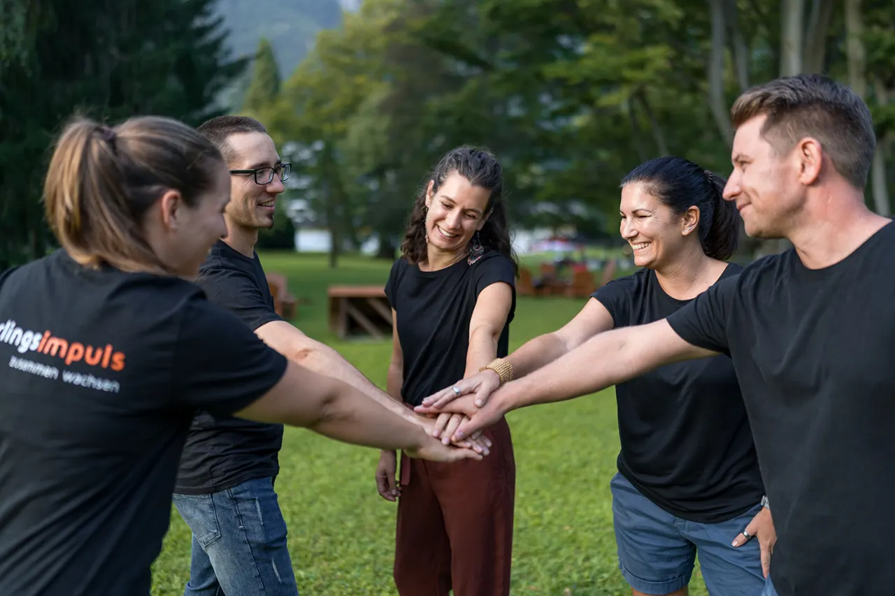 Gruppenfoto der Trainer von Lehrlingsimpuls wie diese die Hände übereinanderlegen um Teamwork und Zusammenhalt zu demonstrieren.