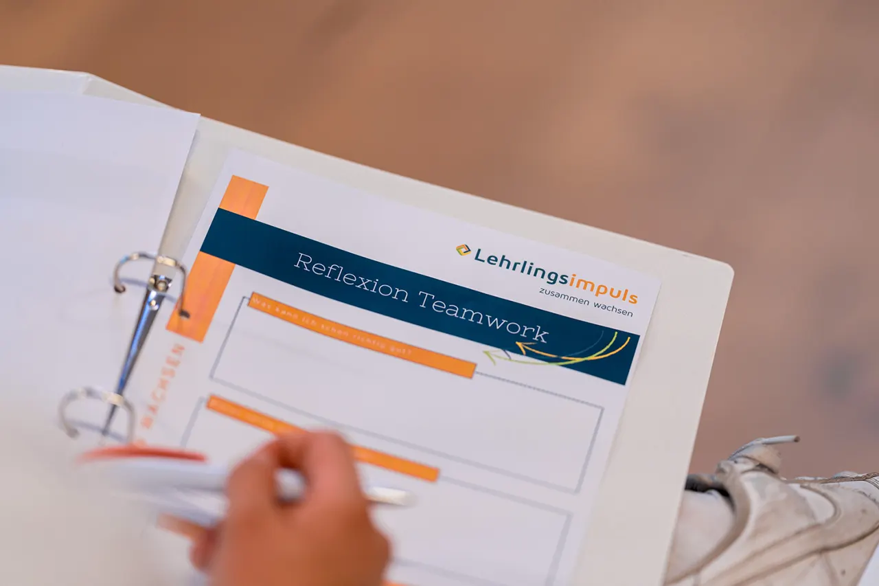 Nahaufnahme eines Lehrlings wie dieser in seine Lehrlingscamp-Mappe von Lehrlingsimpuls Notizen zu dem Thema Teamwork Reflexion schreibt.