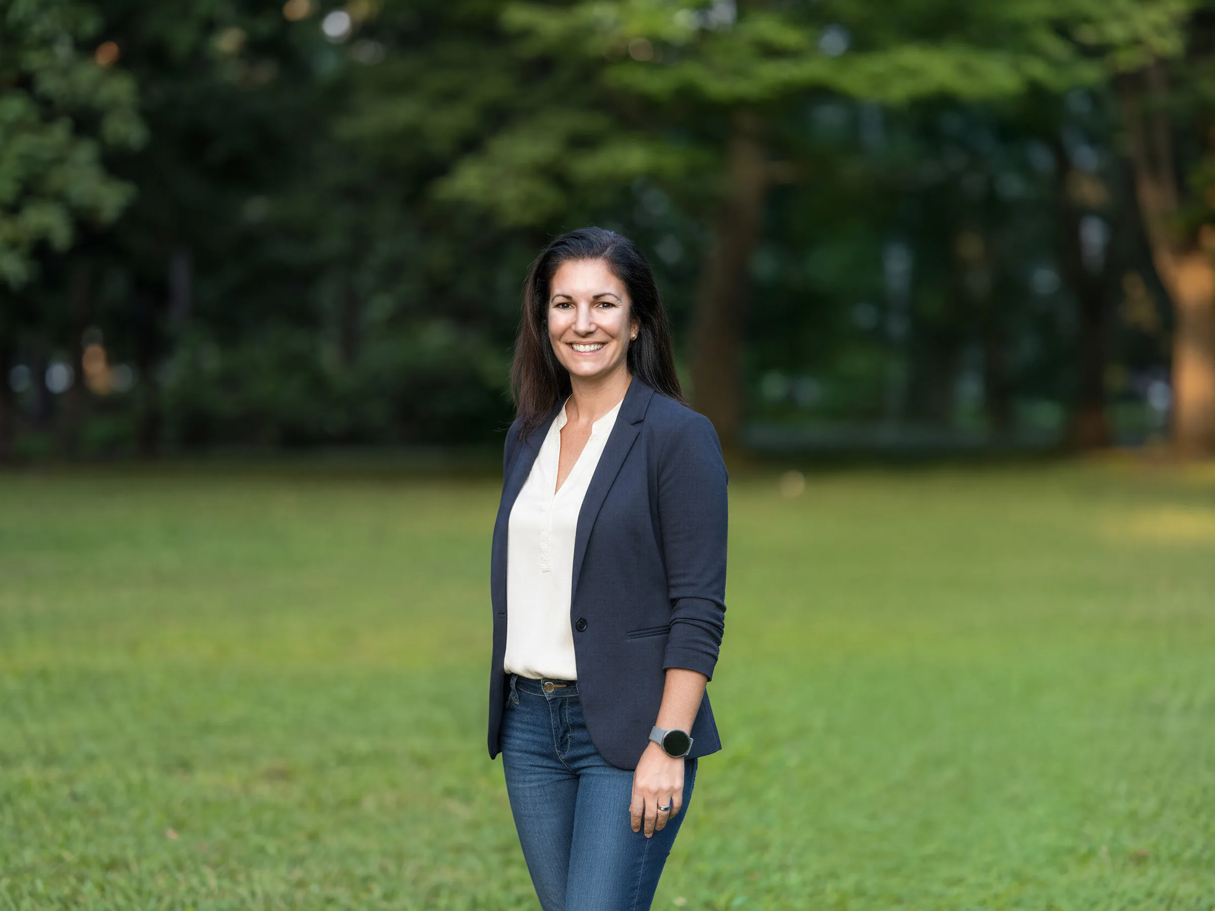 Heike Dormuth, Gründerin von Lehrlingsimpuls, steht lächelnd auf einer grünen Wiese vor Bäumen.