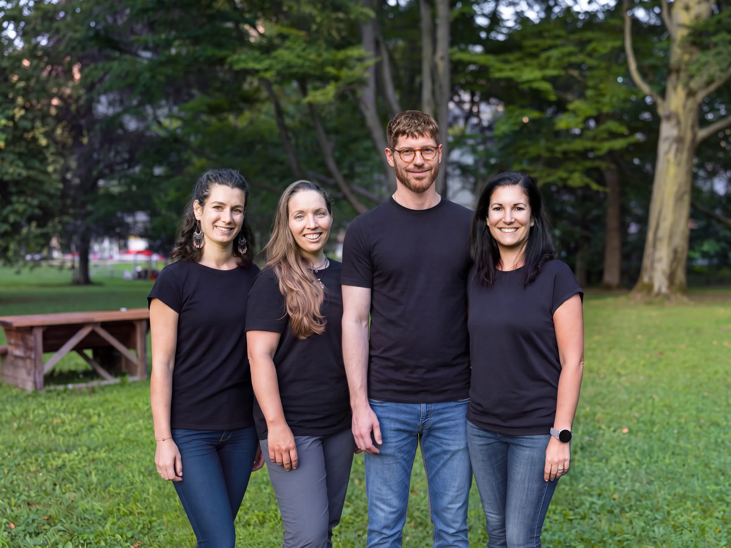 Das Trainer:innen-Team von Lehrlingsimpuls 2026: vier Personen in schwarzen T-Shirts stehen lächelnd nebeneinander in einem Park.