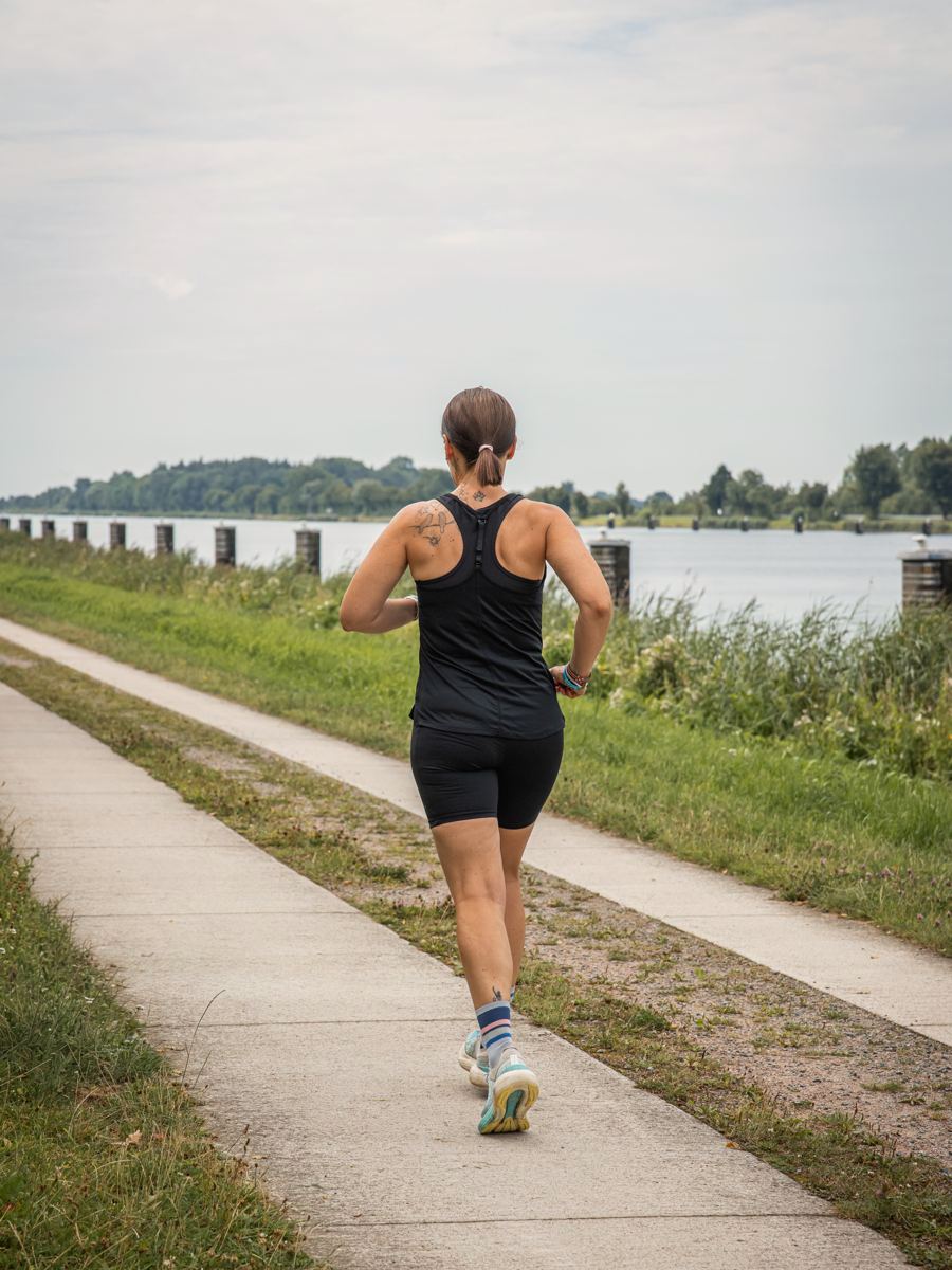 Sabine Pützer von hinten, laufend auf einem Weg am Wasser