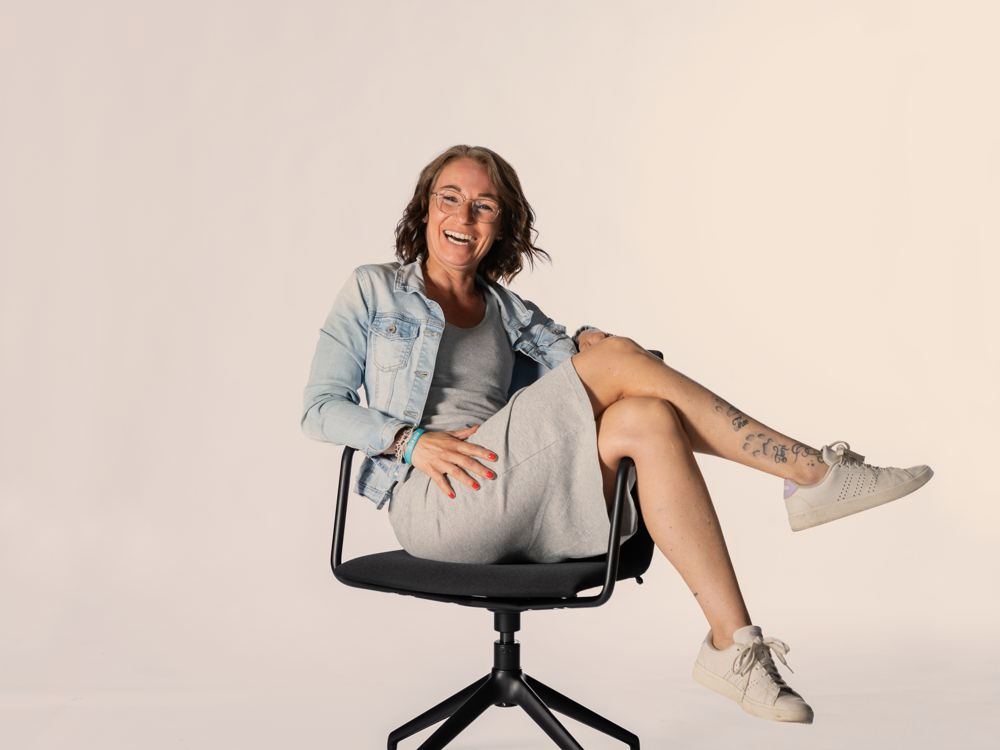 Sabine Pützer lacht auf einem Bürostuhl