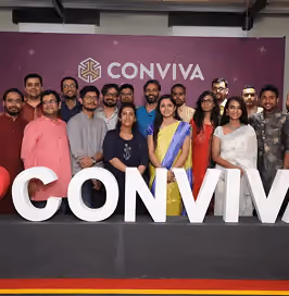 Group of smiling diverse people standing together behind large white letters spelling CONVIVA, with a purple background displaying the Conviva logo above them.