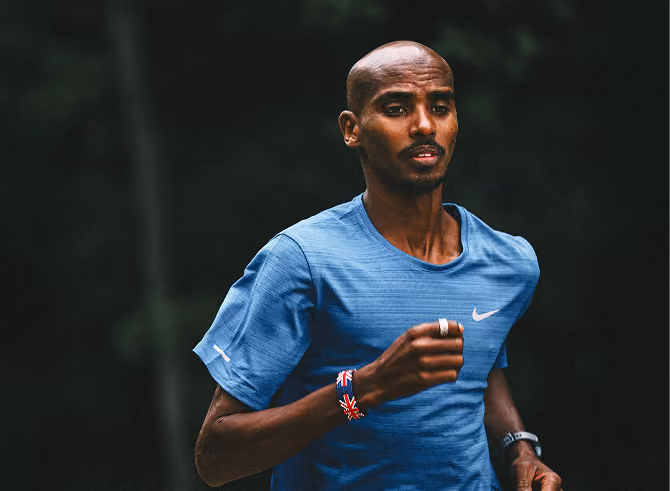 Man wearing a blue Nike running shirt jogging outdoors with a focused expression, against a dark blurred background.
