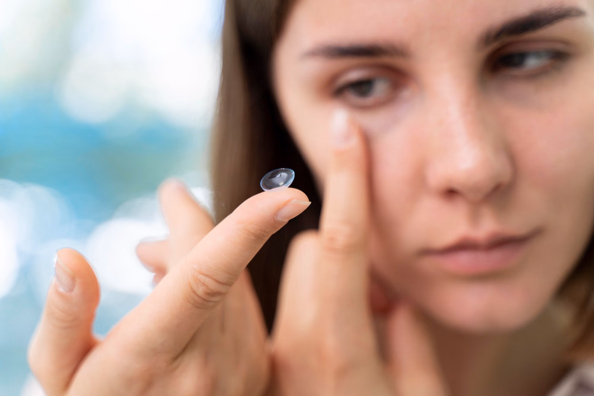 Close-up of a woman holding a contact lens on her fingertip while preparing to put it into her eye.
