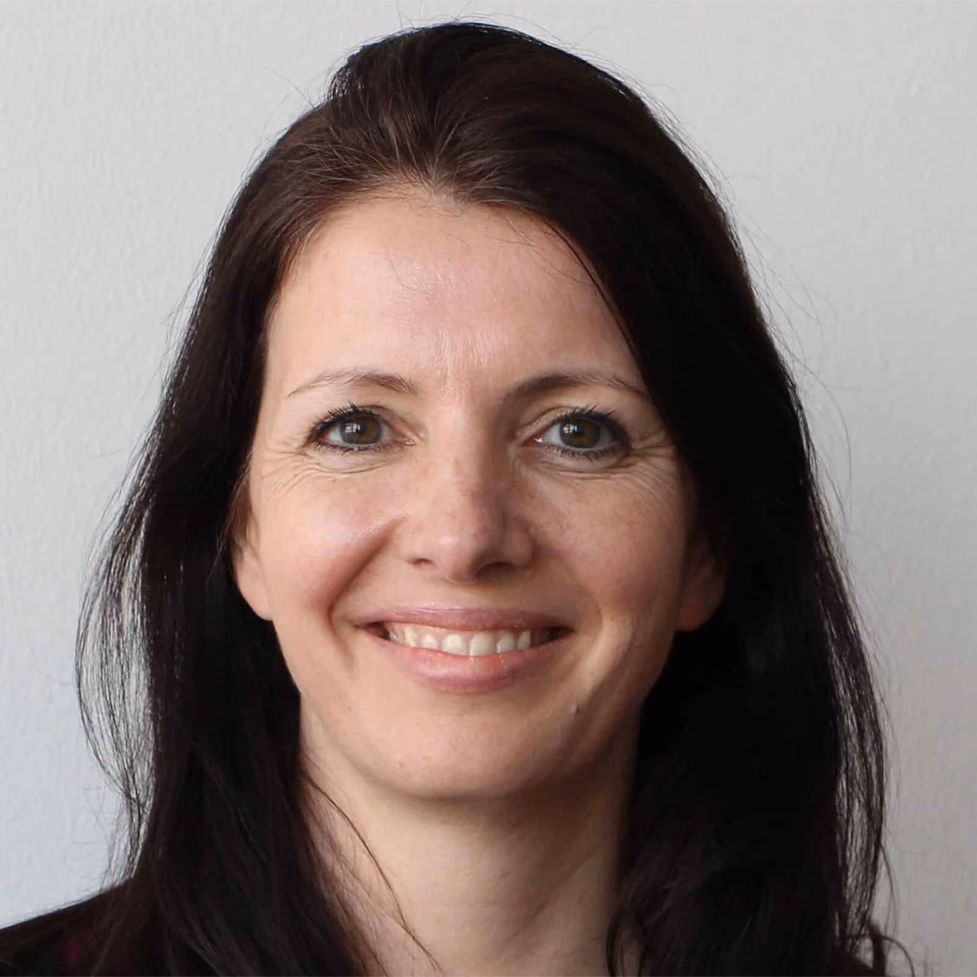 Porträt von Andrea Schwarz mit langen dunklen Haaren vor weißem Hintergrund.