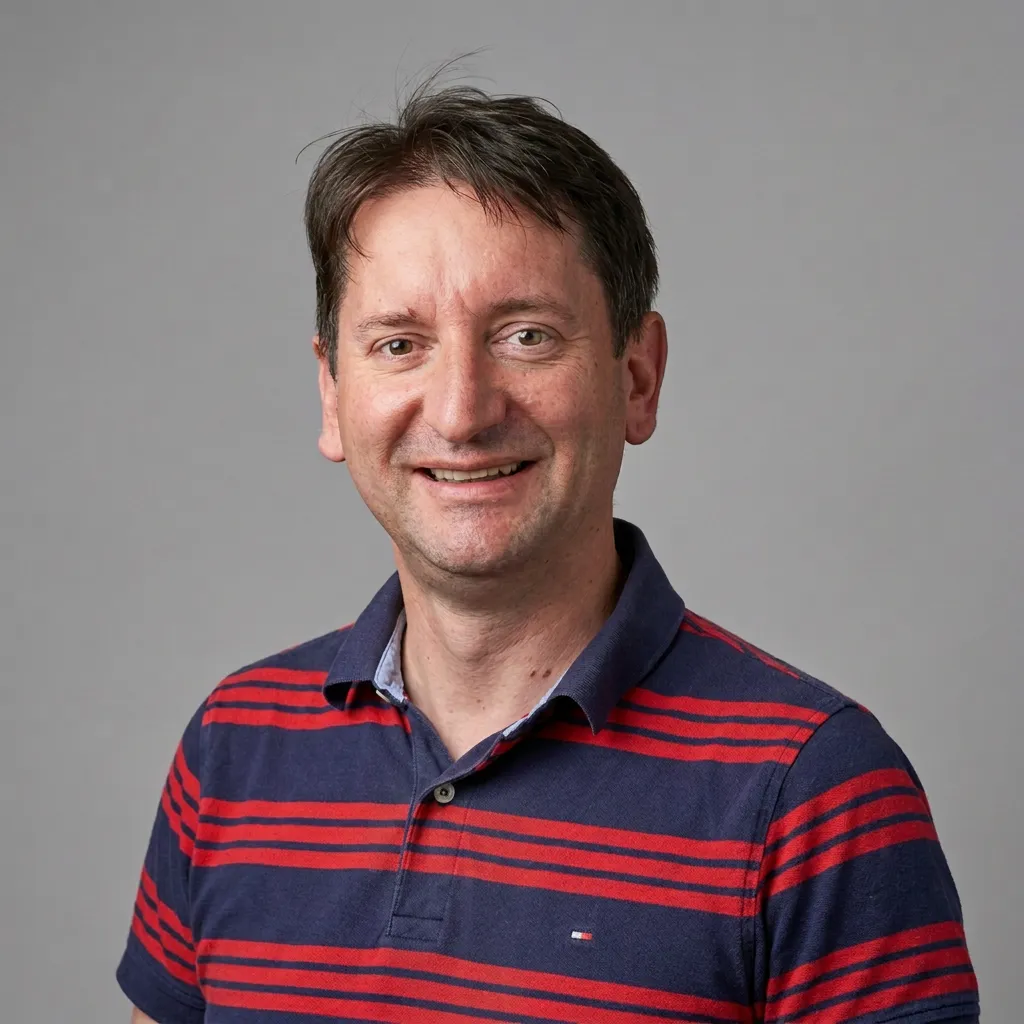 Alexander Schwarz mit mittellangem, lockigem braunem Haar, der lächelt und einen schwarzen Pullover trägt, vor einem neutralen grauen Hintergrund.
