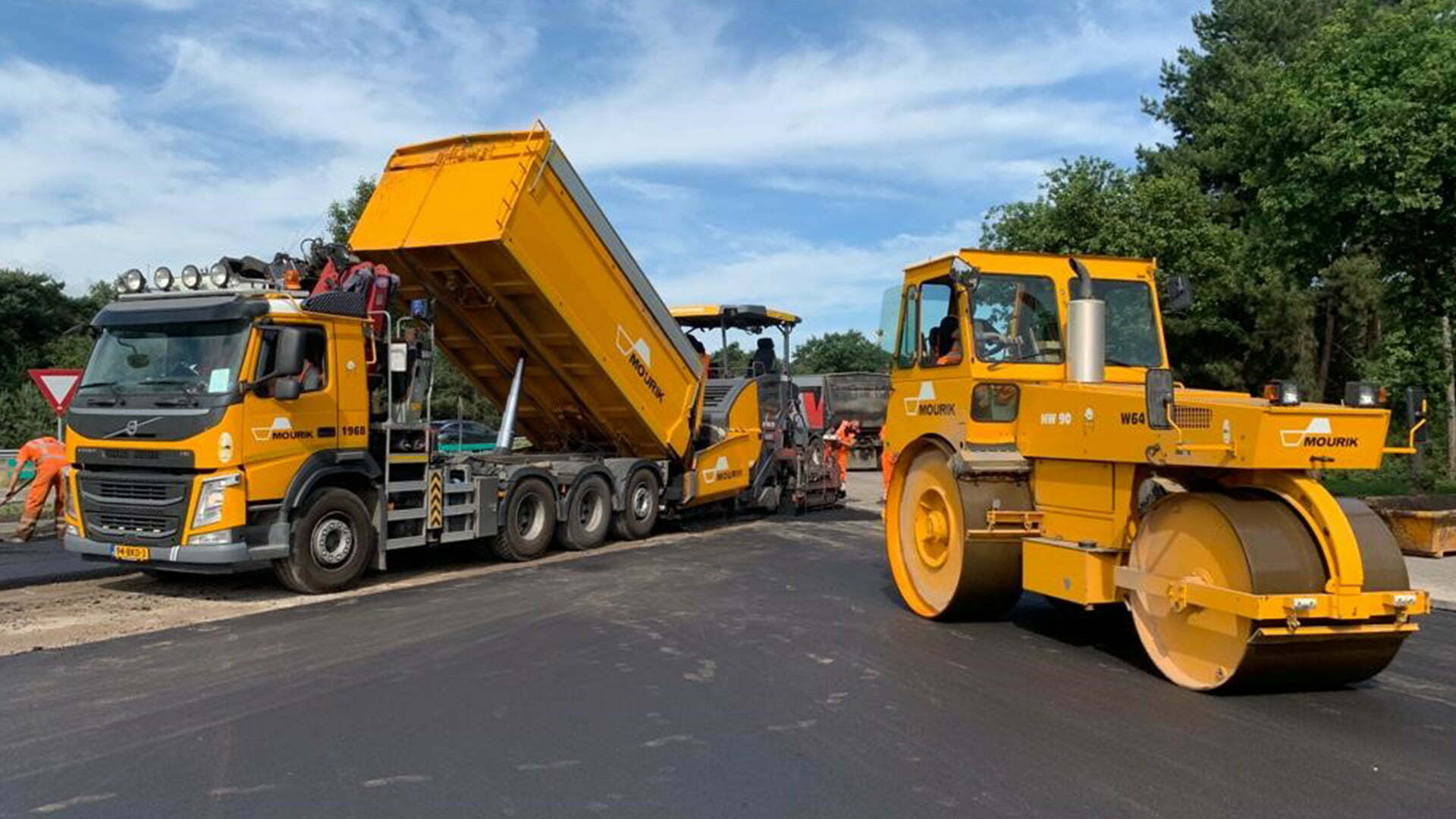 Asphalt machines and a yellow lorry at work on a road