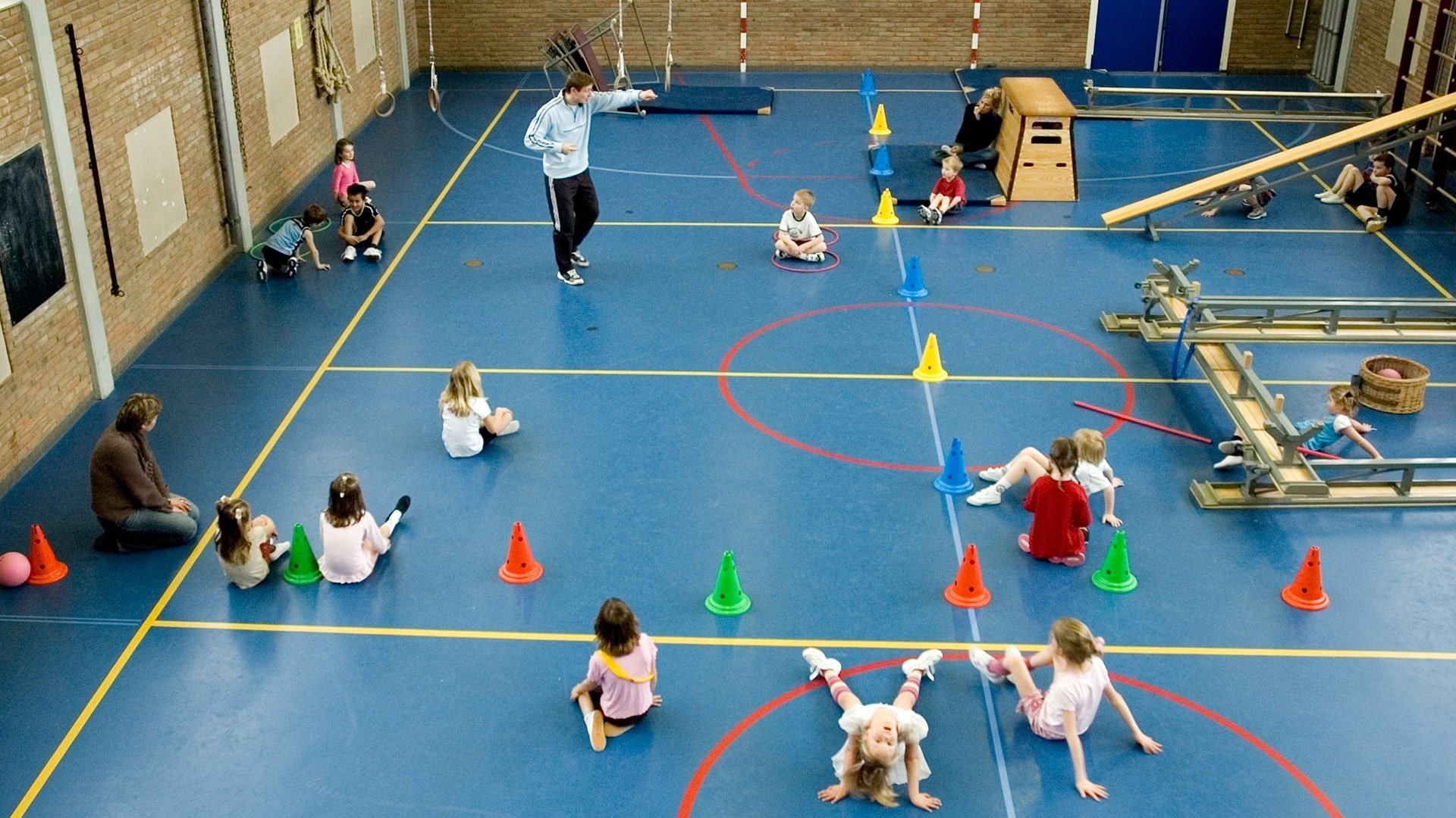 Children doing a PE lesson in a sports hall with cones
