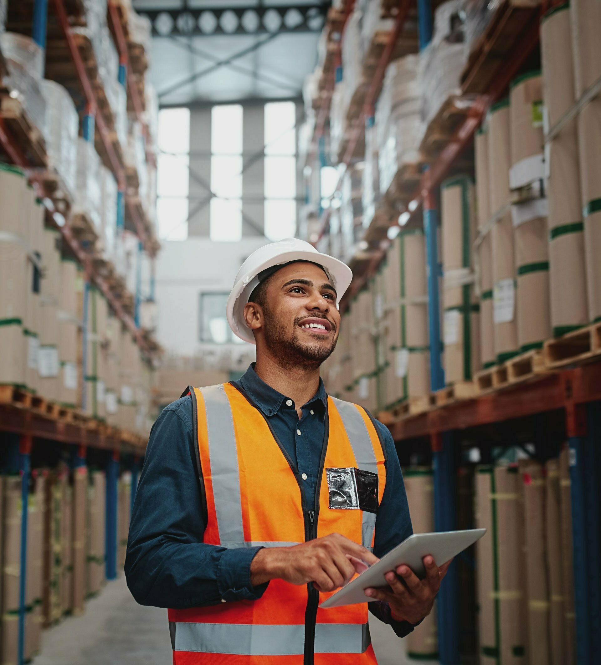 Worker with a white hard hat, orange high-vis vest and tablet in a warehouse