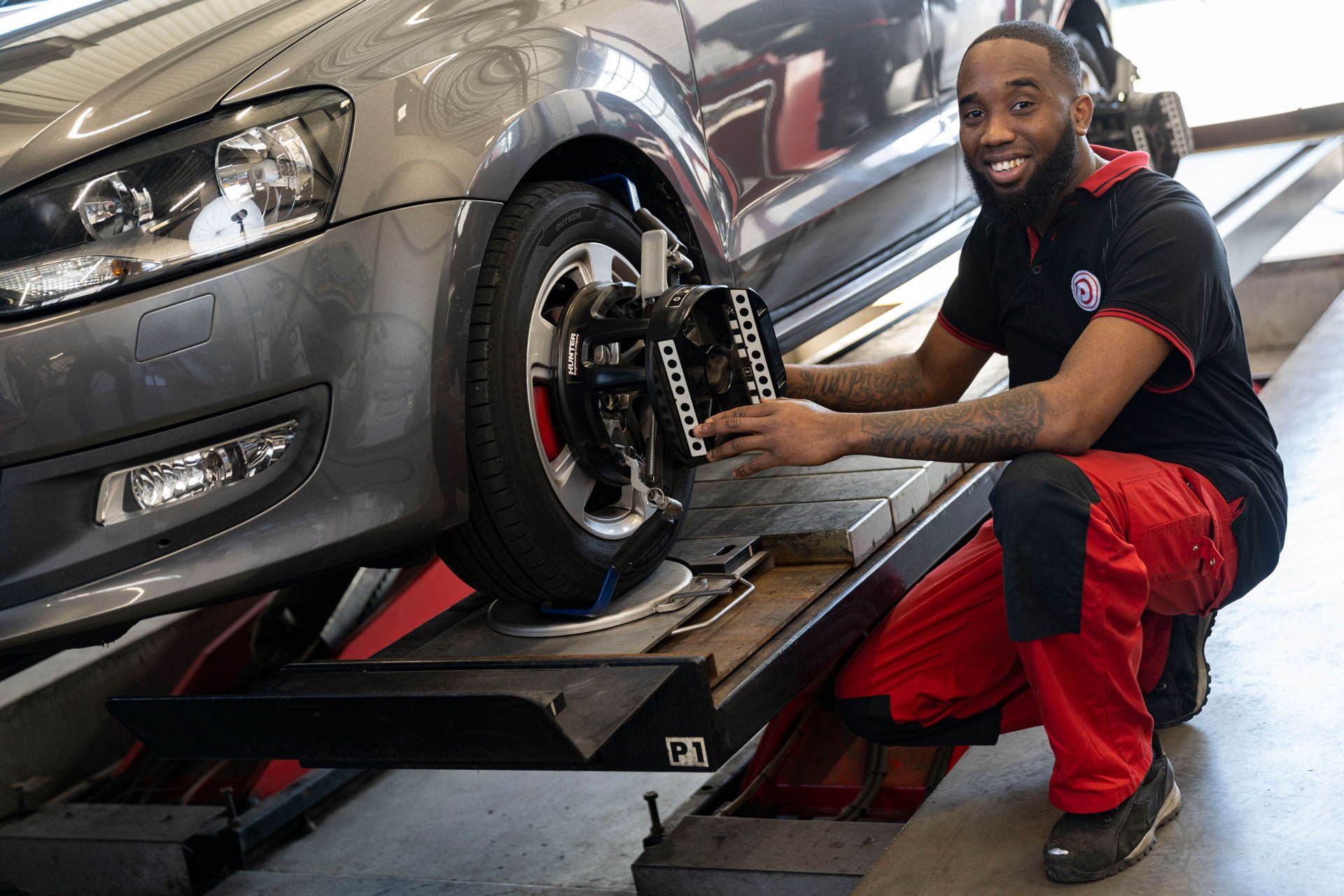 Mechanic in red work trousers crouching by the wheel of a car on a lift