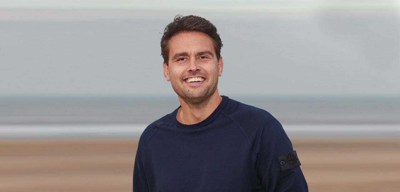 Noud Baijens smiling in a navy jumper in front of a blurred beach