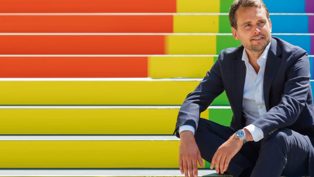 Noud Baijens in a suit sitting on rainbow-coloured stairs