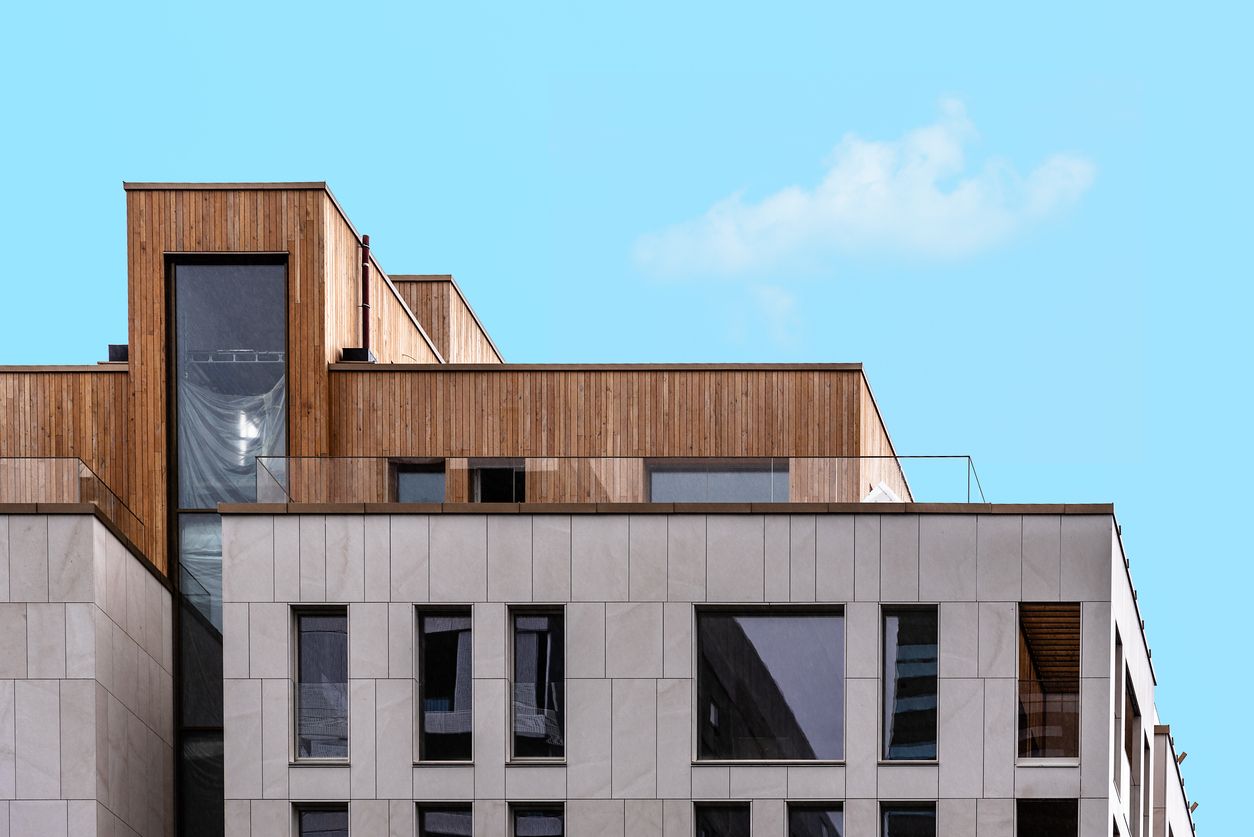 Modern apartment building with wooden and light facade panels against a blue sky