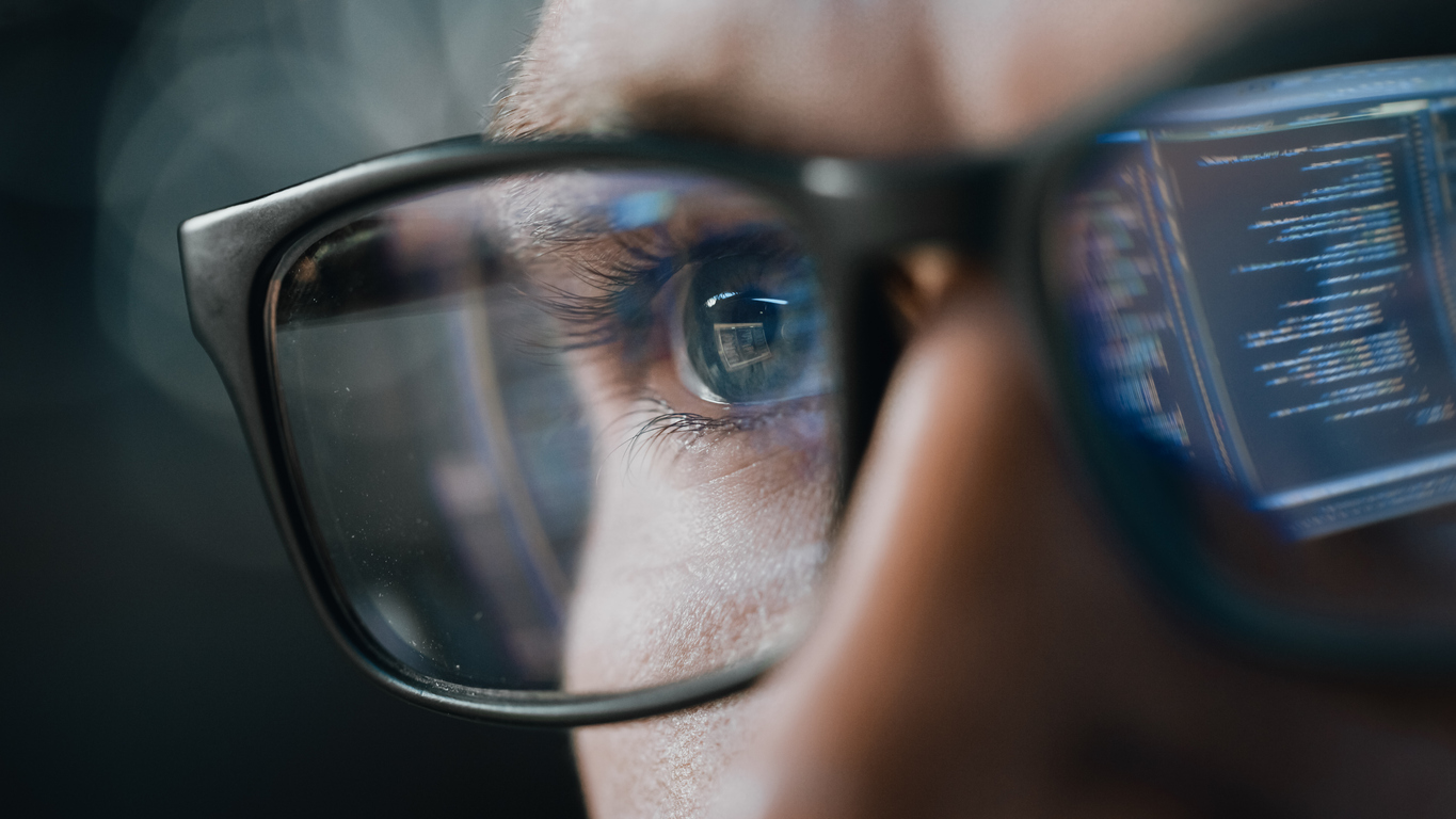 Close-up of a face wearing glasses with programming code reflected in the lenses