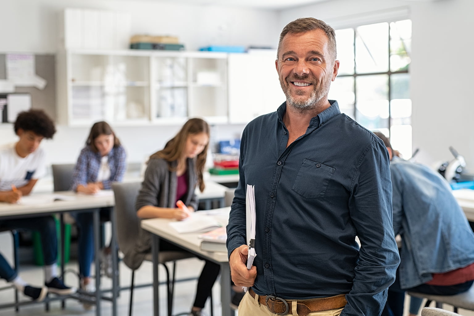 Teacher smiling in a classroom, pupils working at their desks in the background