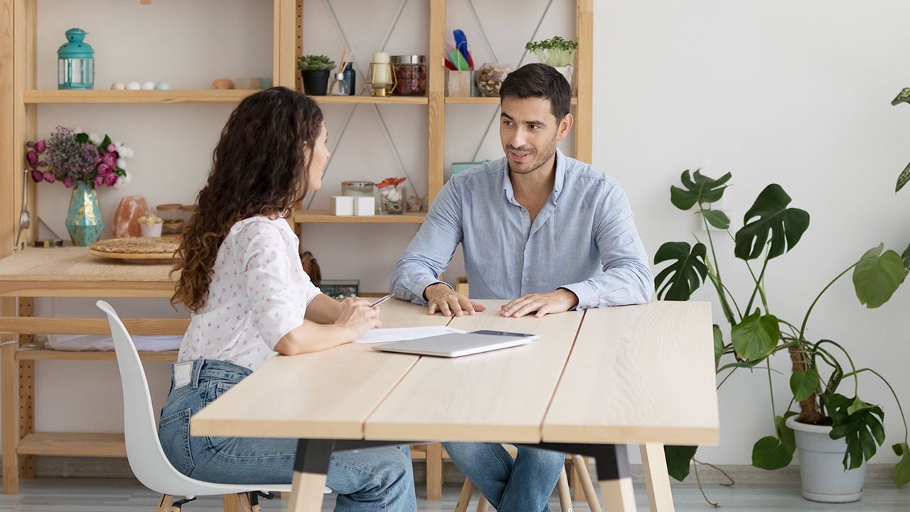 Man and woman talking at a wooden table with a laptop during a job interview