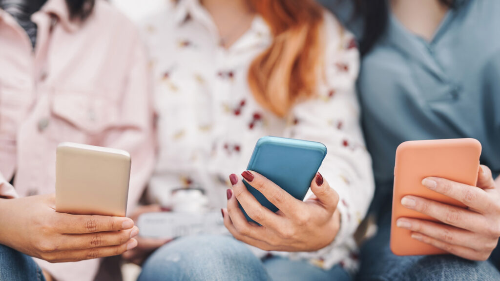 Three young people sitting side by side, each holding a smartphone