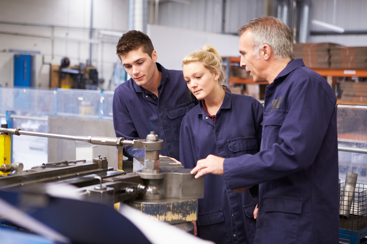 Instructor teaching two young colleagues in overalls to work with a bending machine