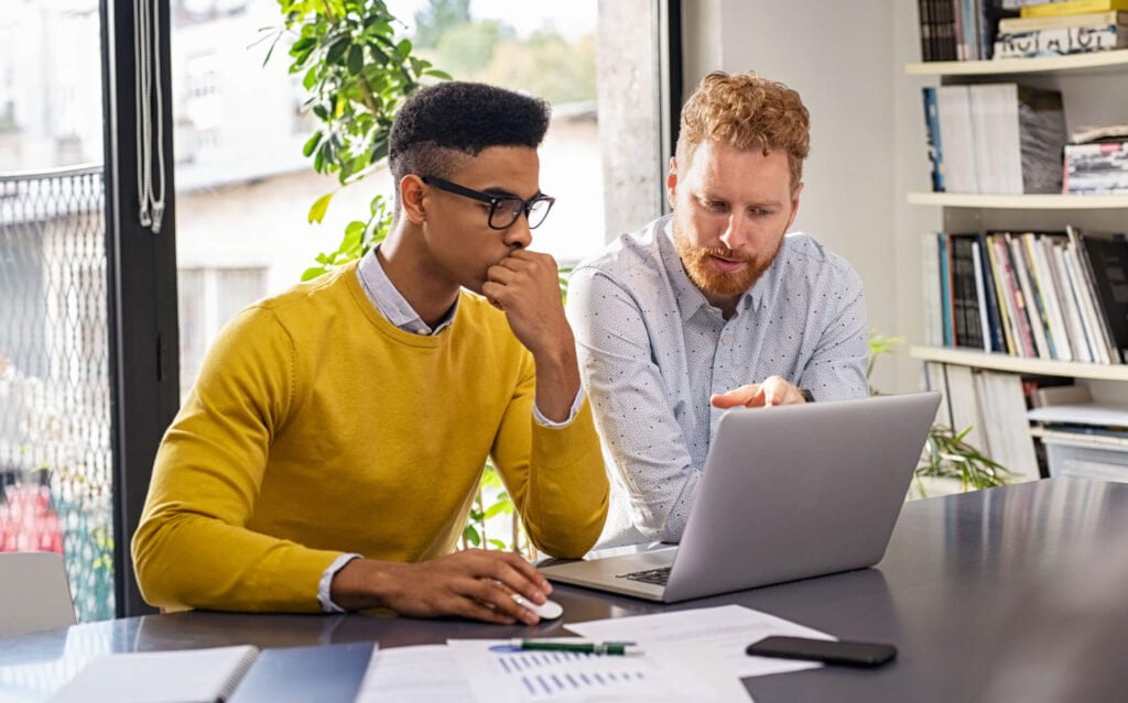 Two colleagues looking at a laptop together at a desk with papers