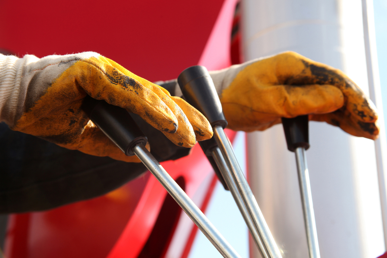 Two hands in yellow work gloves operating the levers of a crane