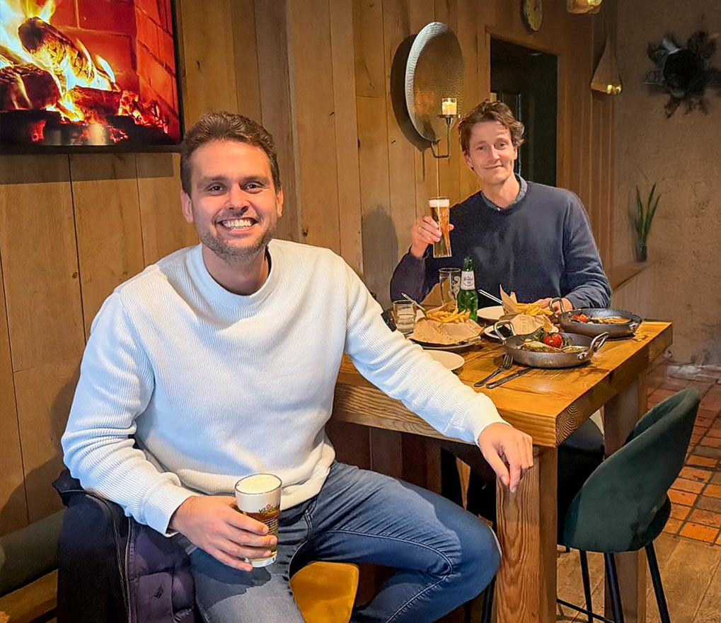 Two men at a wooden table in a restaurant with beer and hot dishes