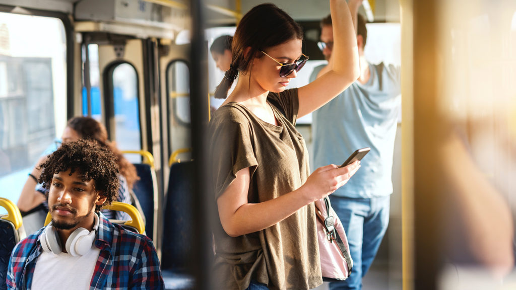 Young woman on a bus looking at her phone, with other passengers around her