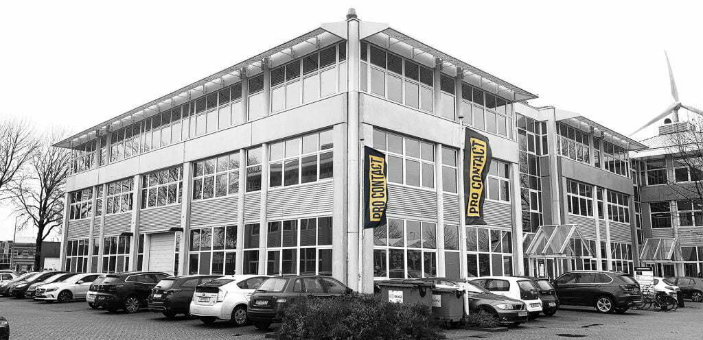 Black and white photo of an office building with two Pro Contact flags, cars in the car park in front