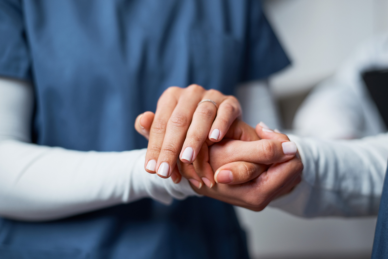 Nurse in blue scrubs holding a patient's hand