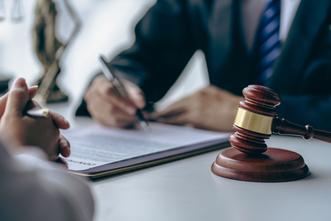 Wooden gavel on a table while someone in a suit signs a contract
