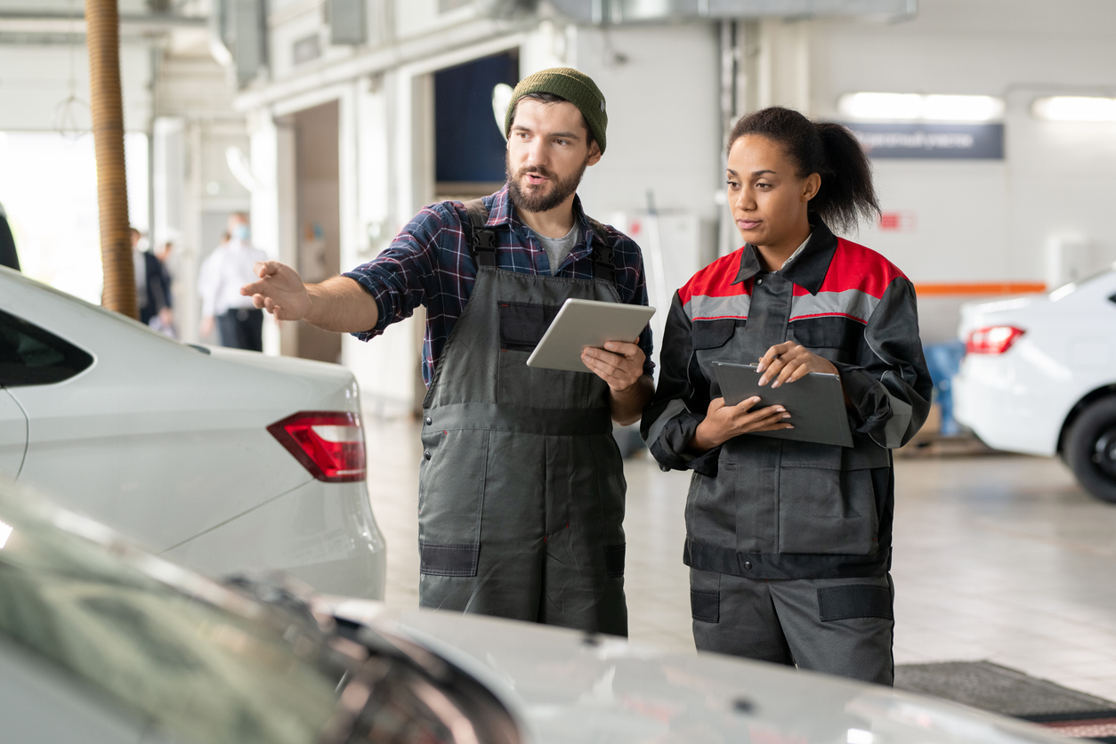 Two mechanics in workwear discussing something on tablets in a car garage