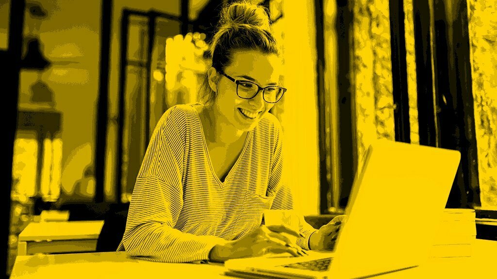Smiling woman with glasses working on a laptop, image tinted yellow