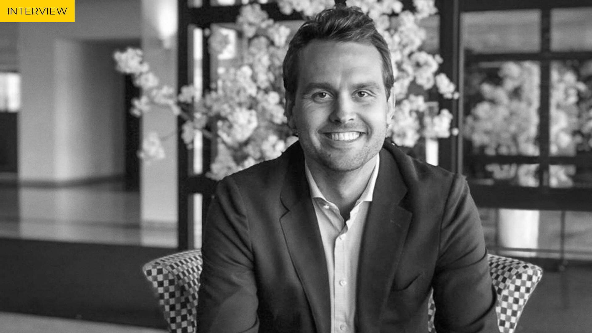Black and white portrait of a smiling man in a blazer, labelled Interview