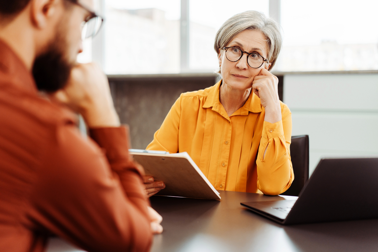 Older woman with glasses listening closely to a man opposite her, with a laptop on the table
