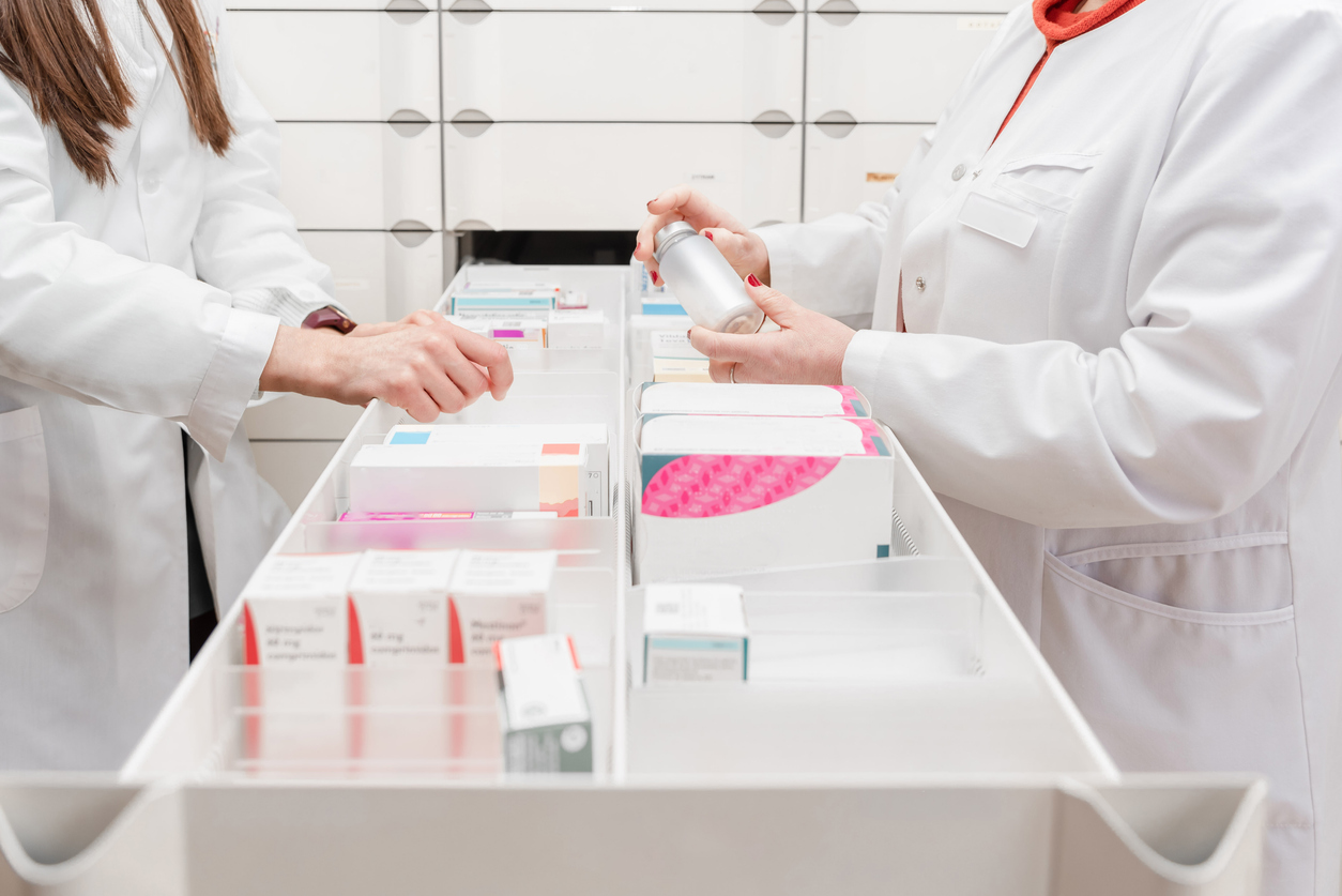 Two pharmacists in white coats sorting medicine boxes in a drawer