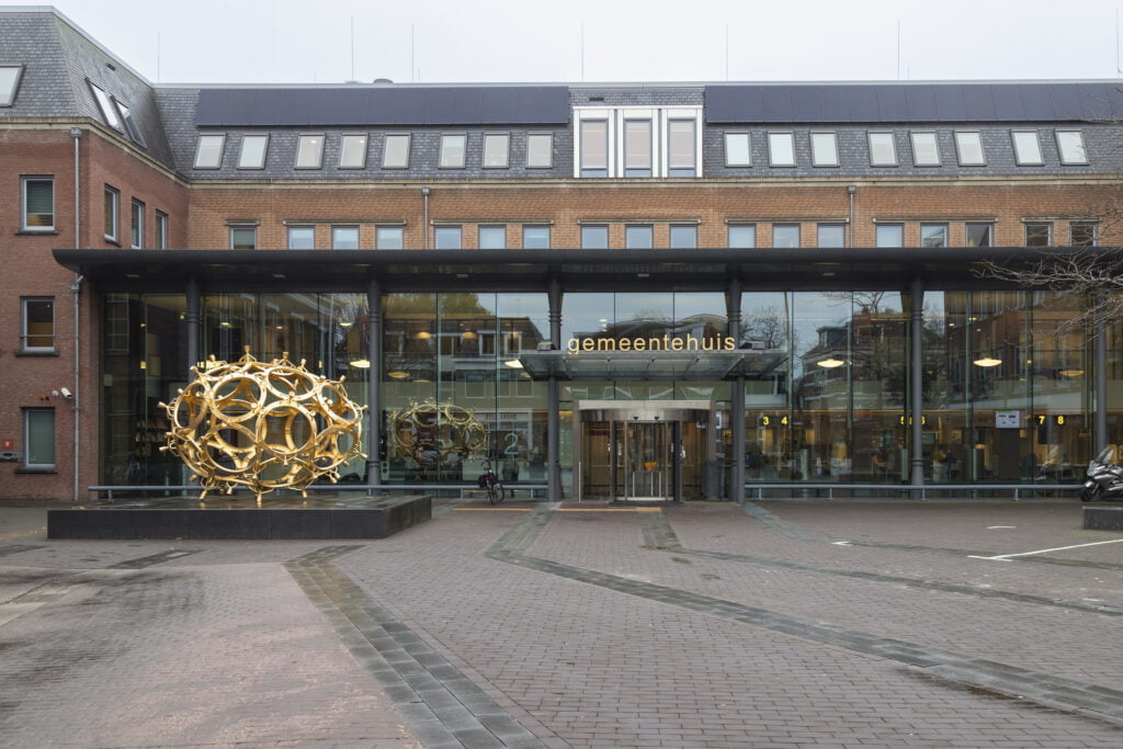 Brick town hall with a glass entrance and a golden artwork on the square in front