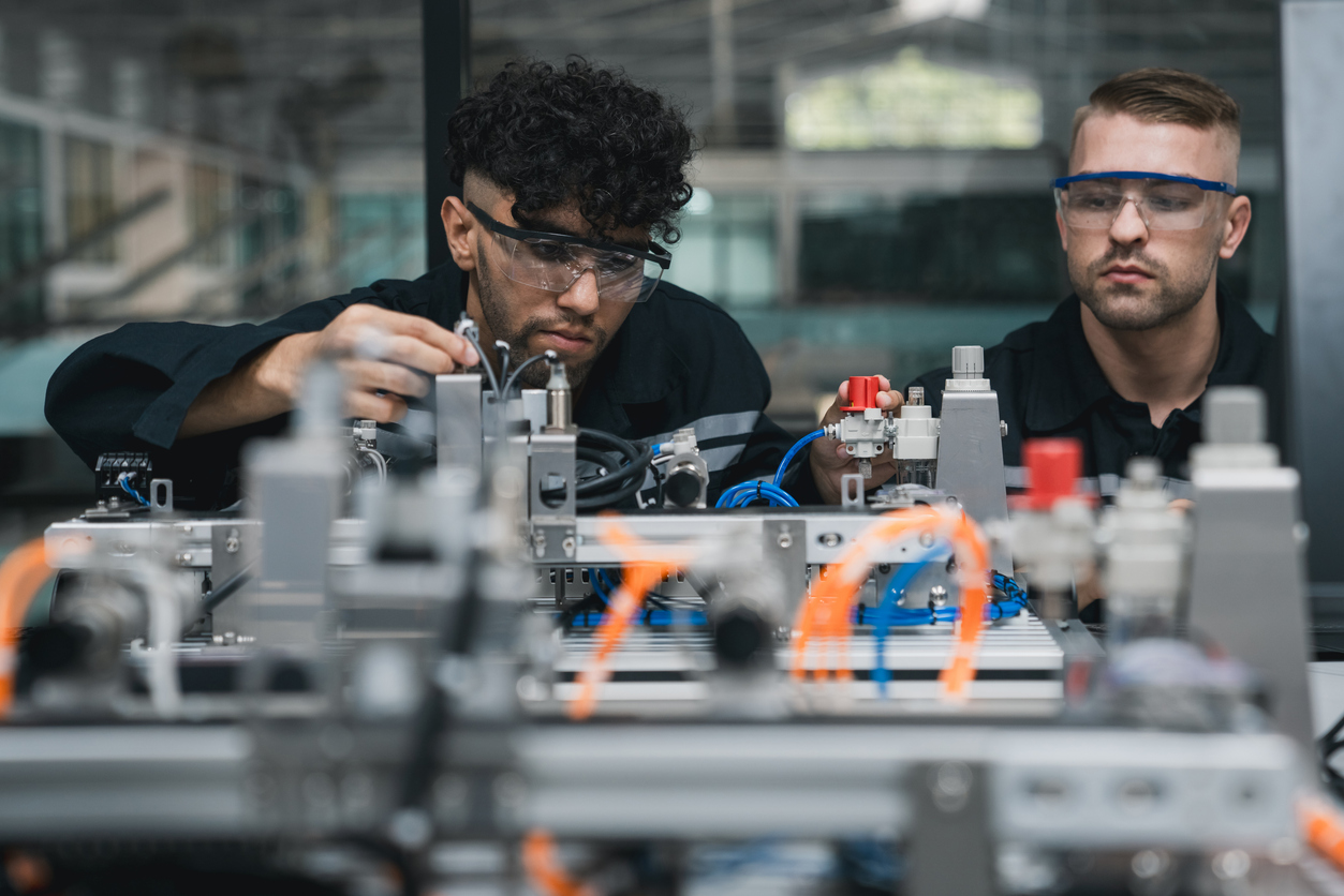 Two technicians wearing safety glasses working on a machine with tubes and parts