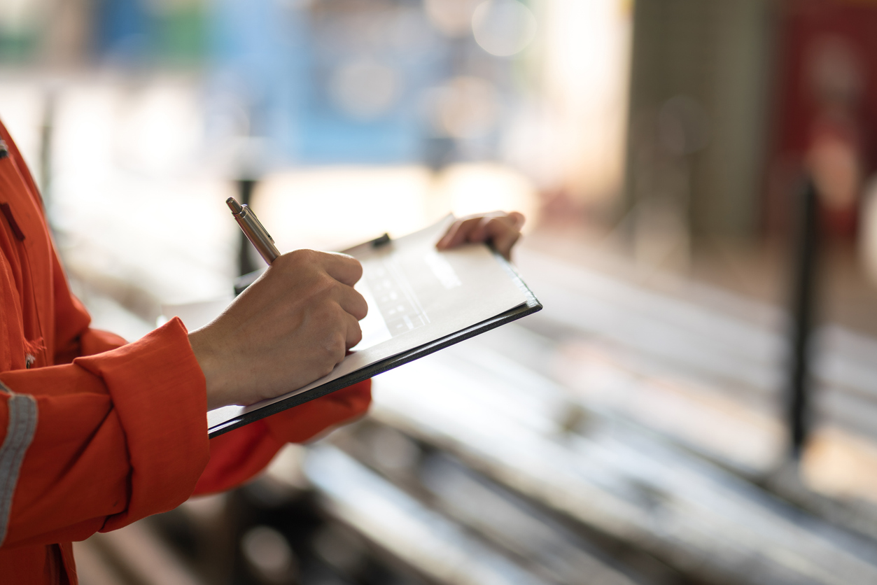 Hand of a person in orange overalls writing on a clipboard