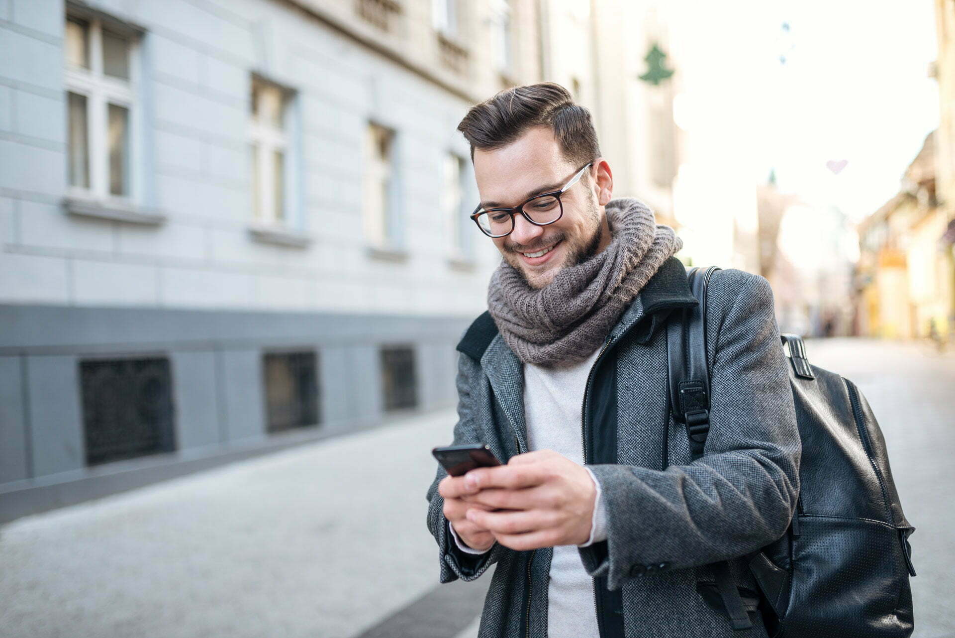 Smiling man with glasses and a scarf looking at his phone in a street