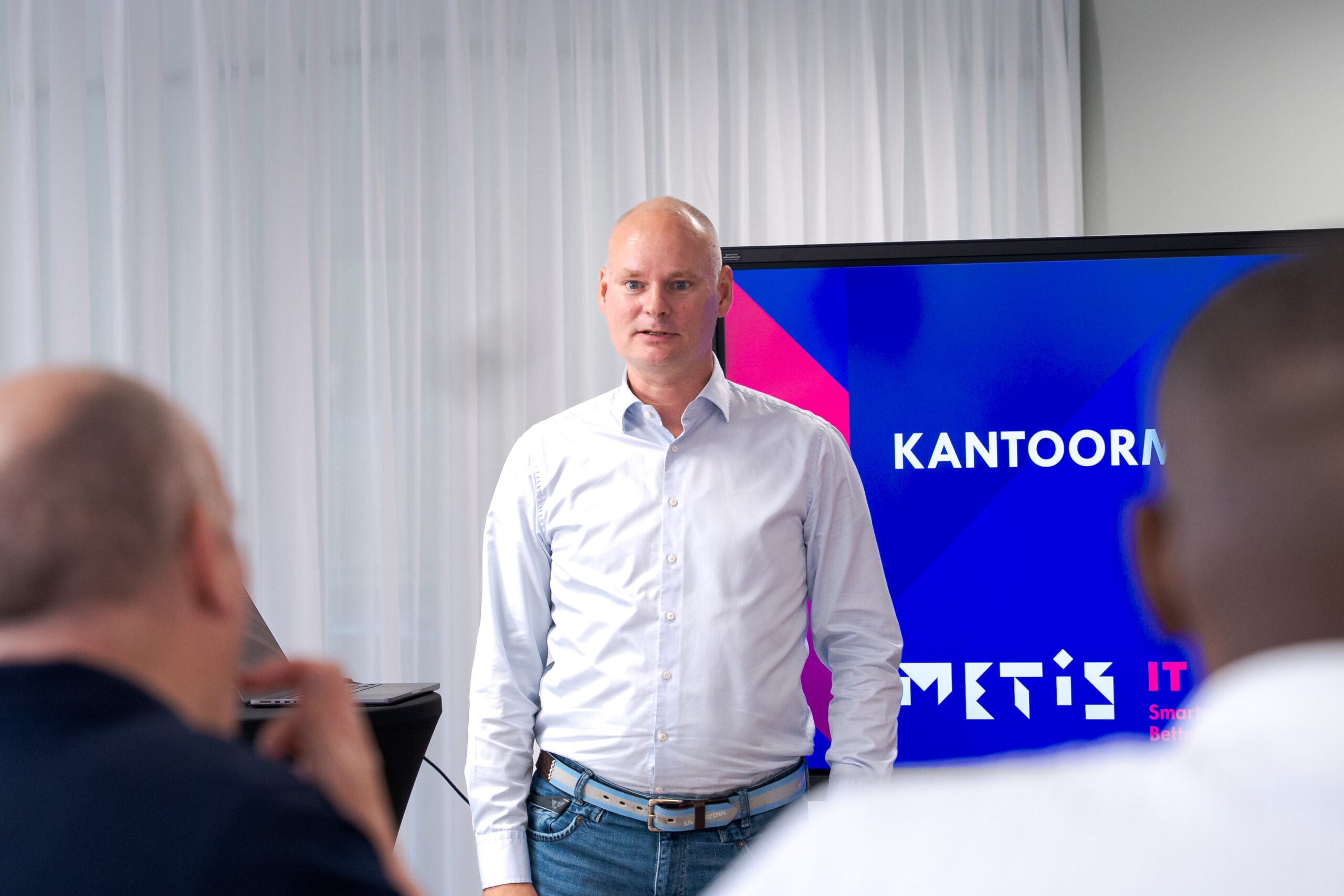 Man in a shirt giving a presentation in an office, with the Metis IT logo on the screen behind him