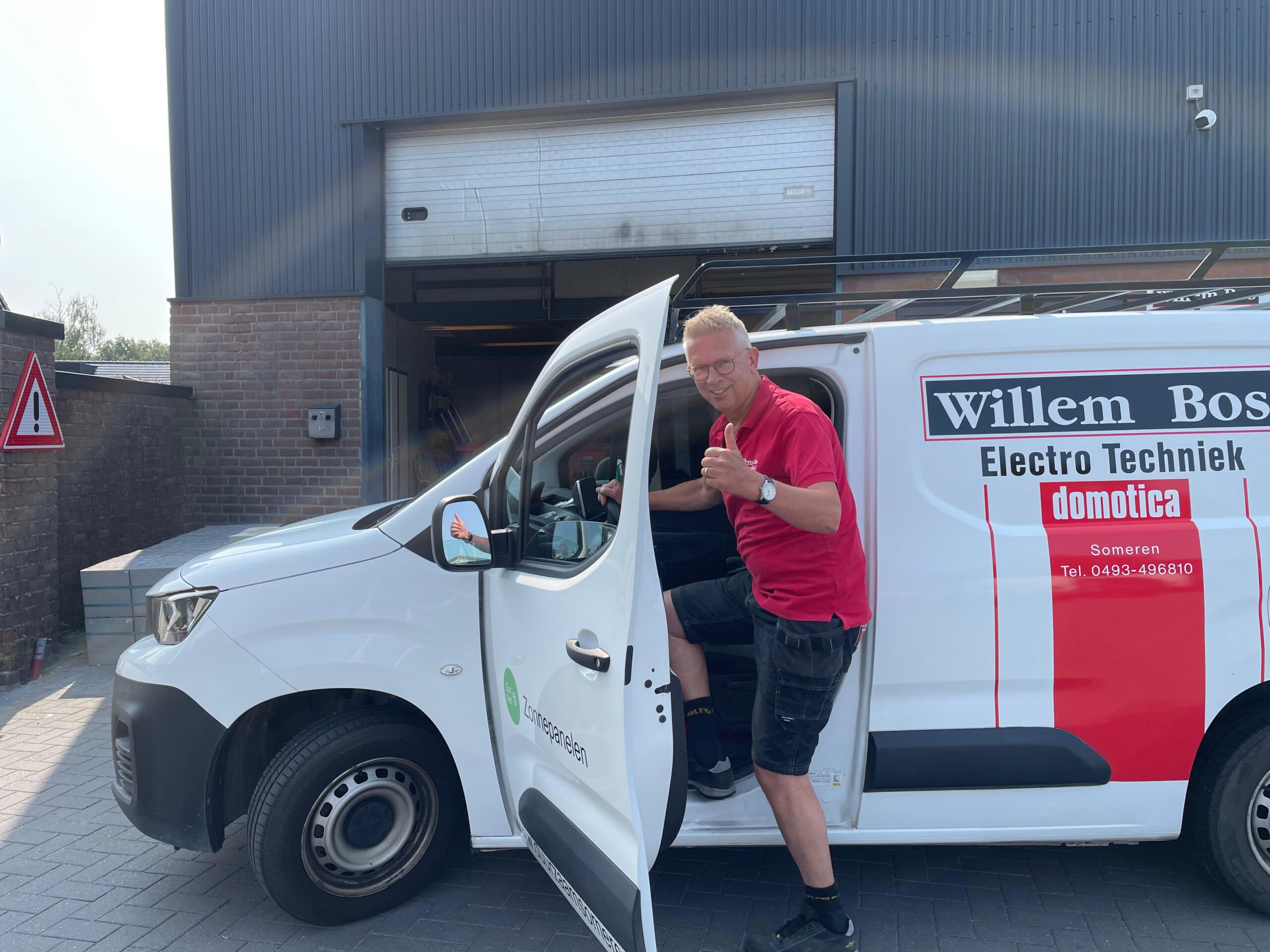 Man in a red polo shirt giving a thumbs up next to a white Willem Bos Electro Techniek van