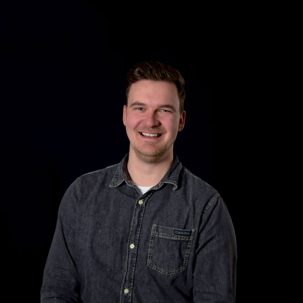 Smiling man in a denim shirt against a black background
