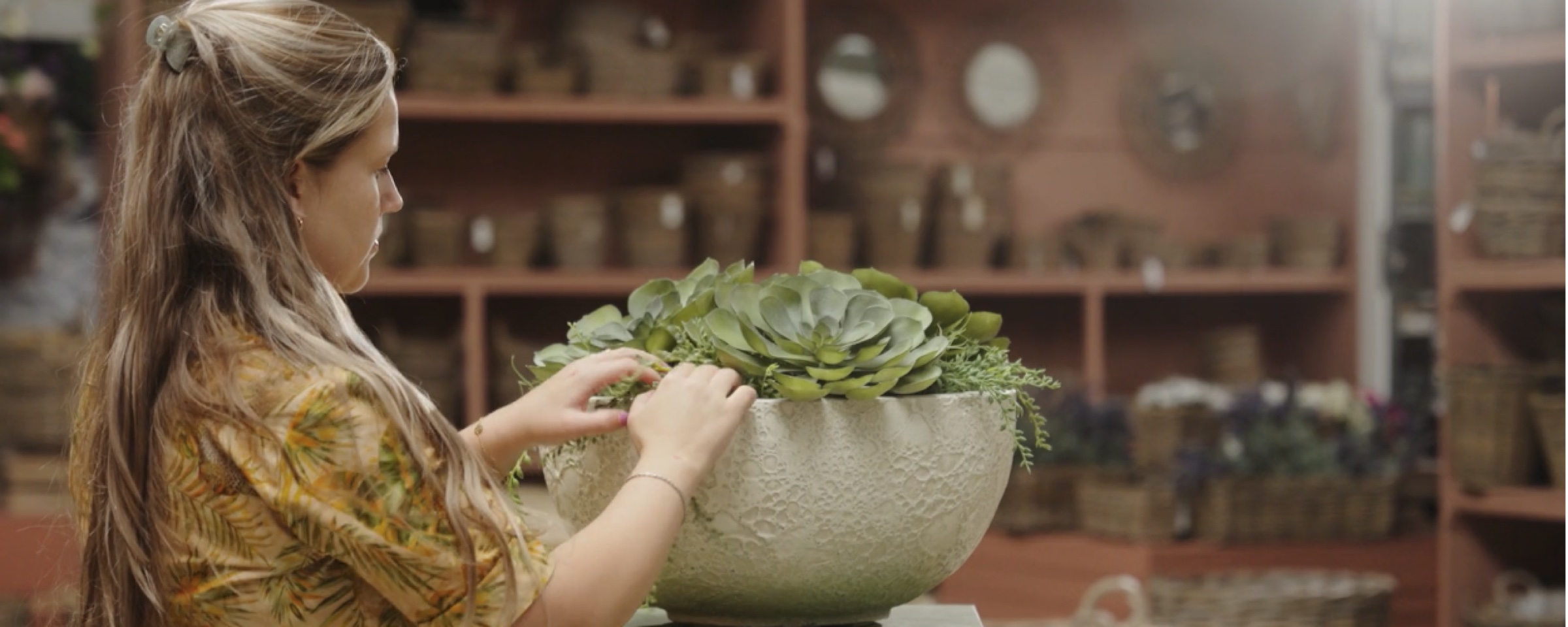 Woman arranging a succulent in a large stone bowl in a shop with pots and baskets