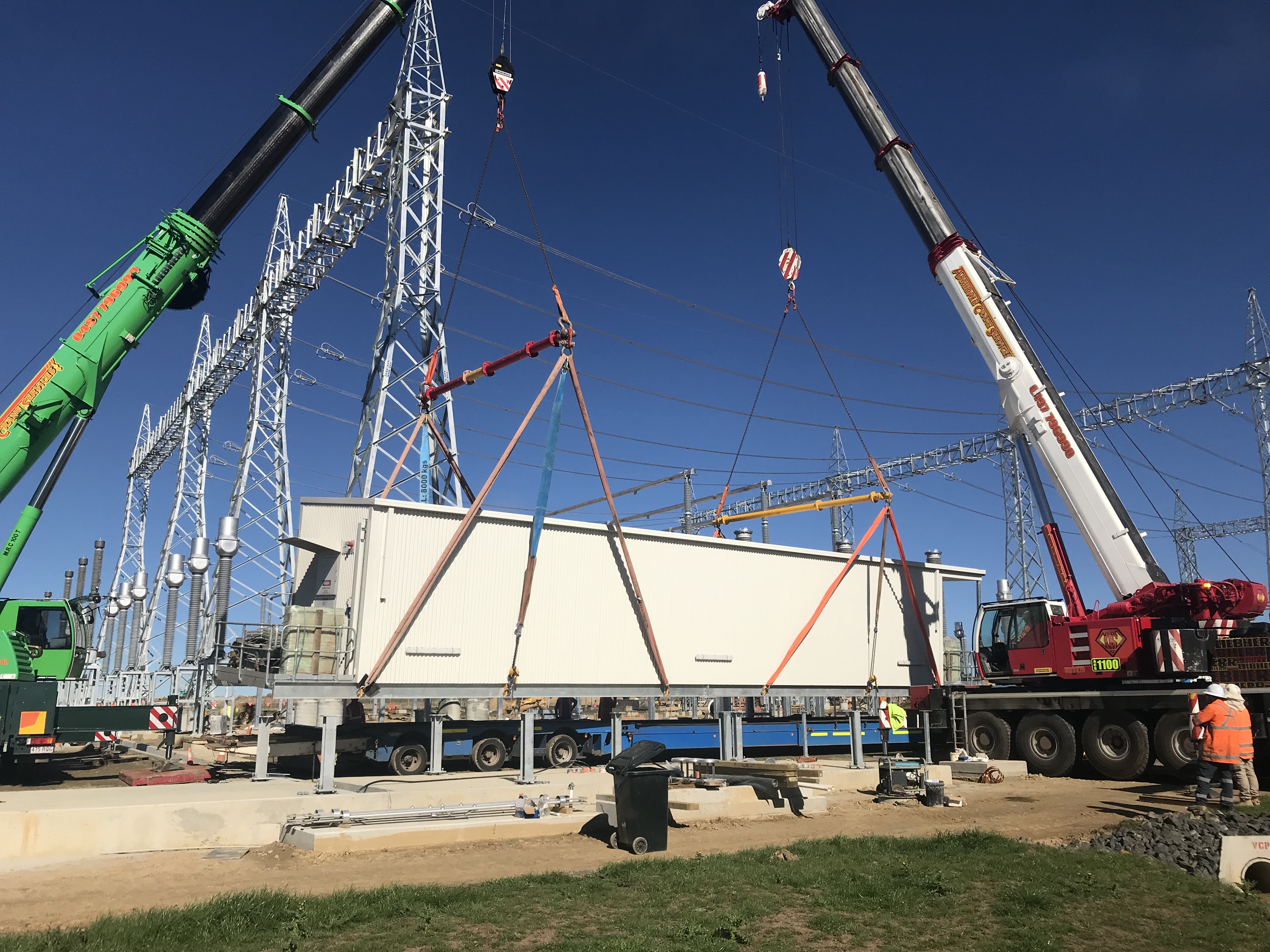 Crane lifting a substation enclosure into place with transmission towers in the background