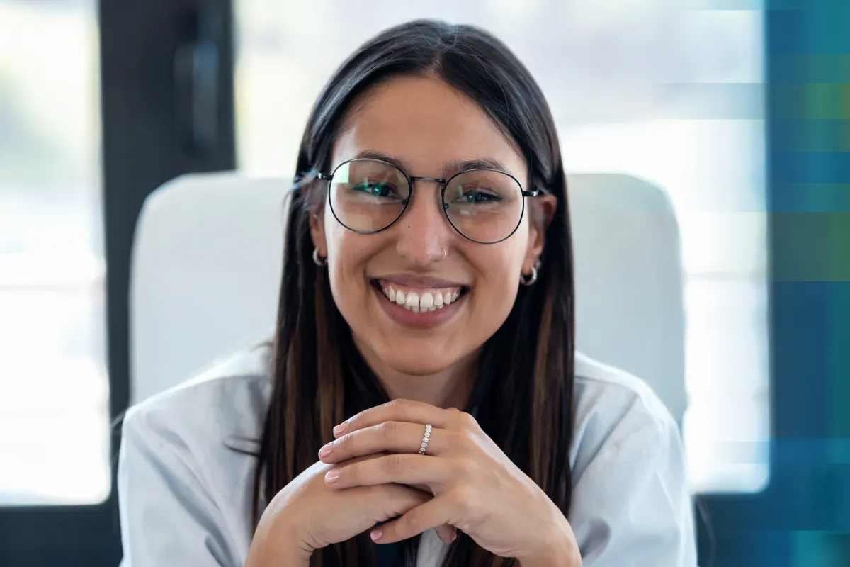 A smiling woman with glasses sitting with her hands clasped