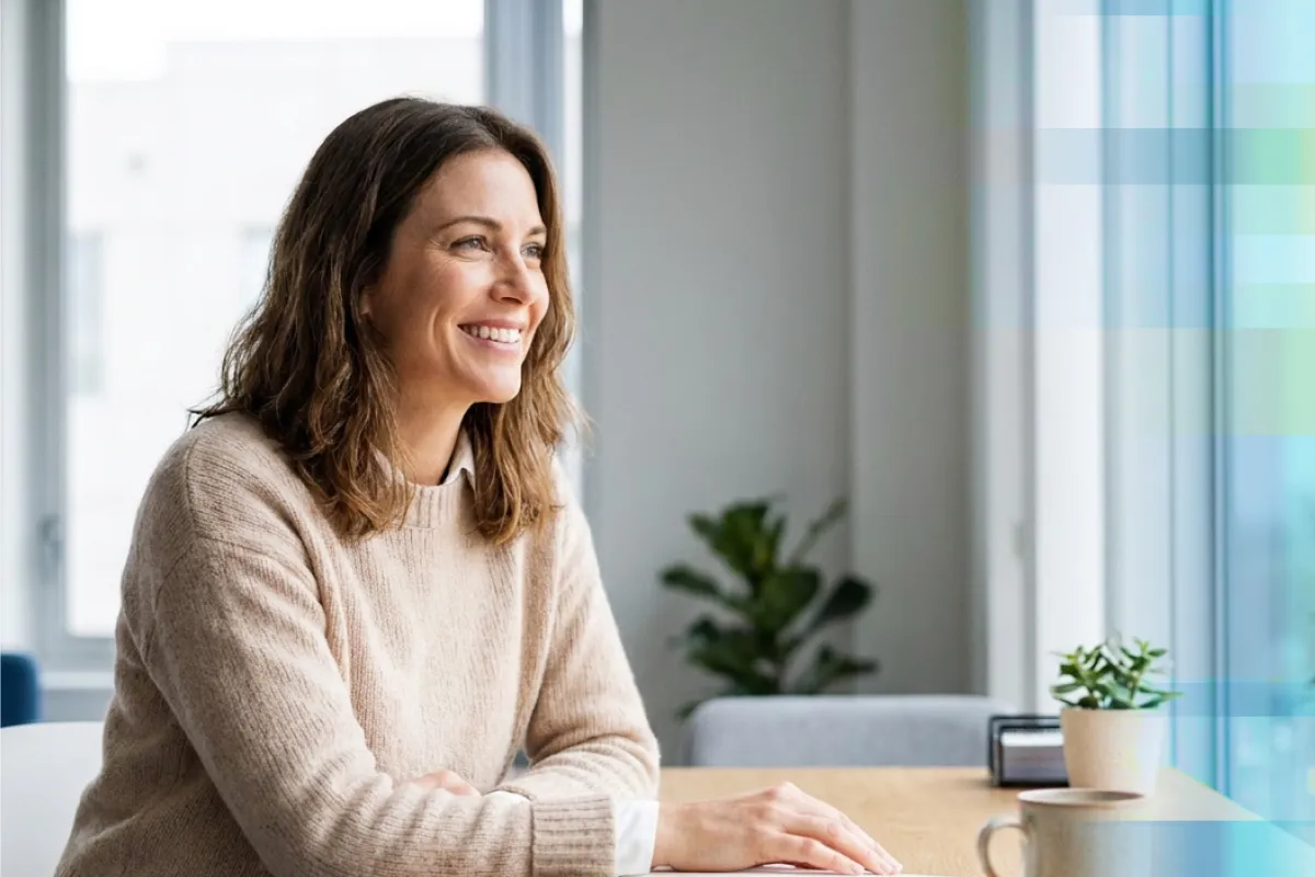 A smiling woman sitting at a table and looking out a window