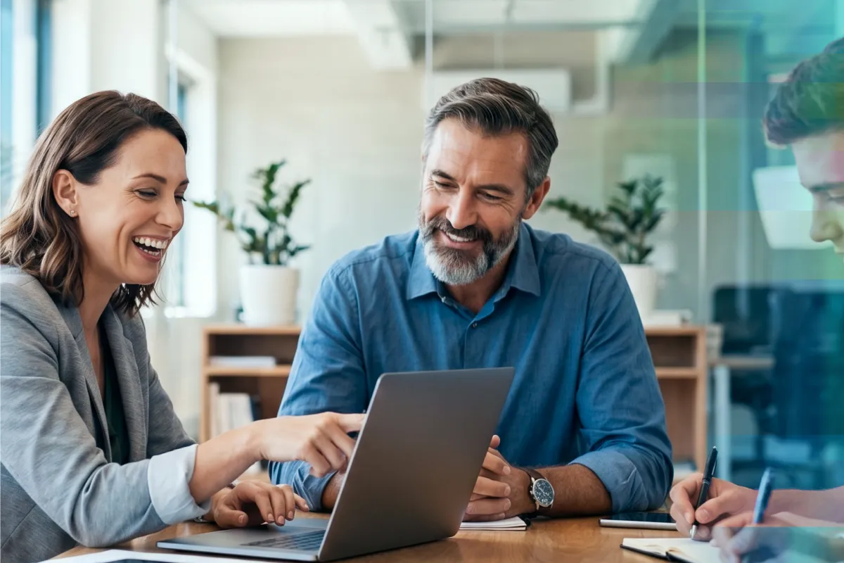 Two coworkers smiling while reviewing information on a laptop together