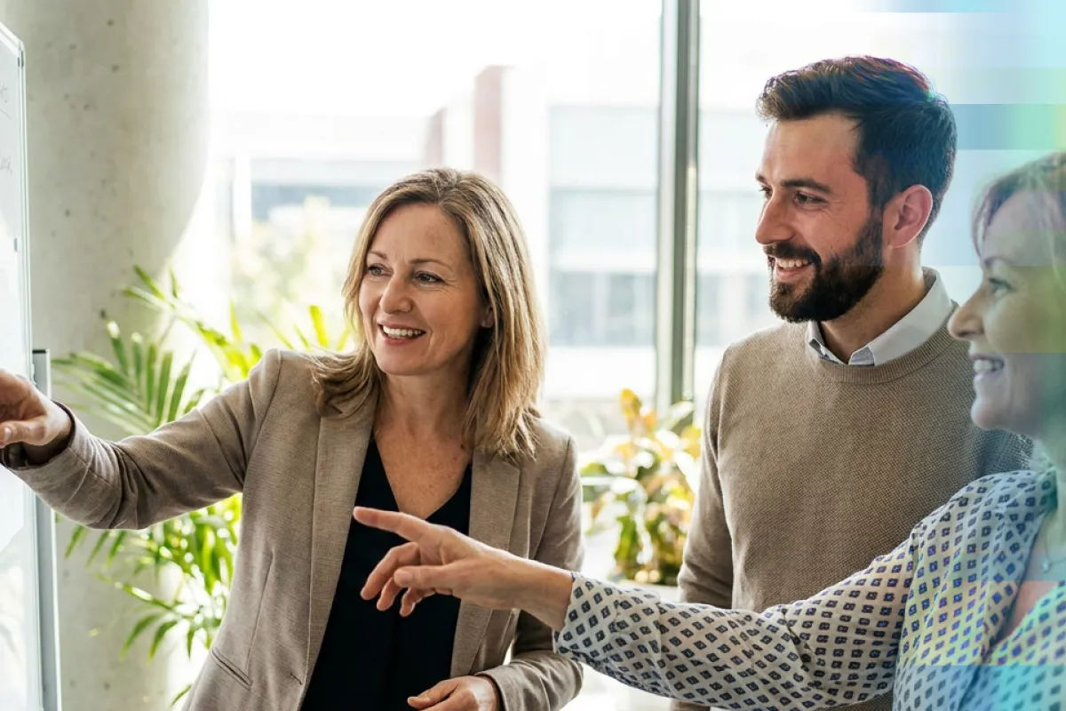 Woman pointing while presenting to smiling colleagues in a plant-filled office