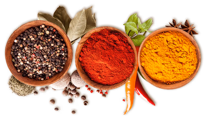 Three wooden bowls filled with whole peppercorns, red chili powder, and turmeric powder, surrounded by garlic cloves, bay leaves, fresh green herbs, star anise, and red chili peppers.