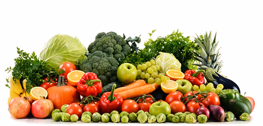 A colorful assortment of fresh vegetables and fruits, including broccoli, carrots, tomatoes, bell peppers, Brussels sprouts, green apples, grapes, pineapple, cabbage, and onions arranged against a white background.